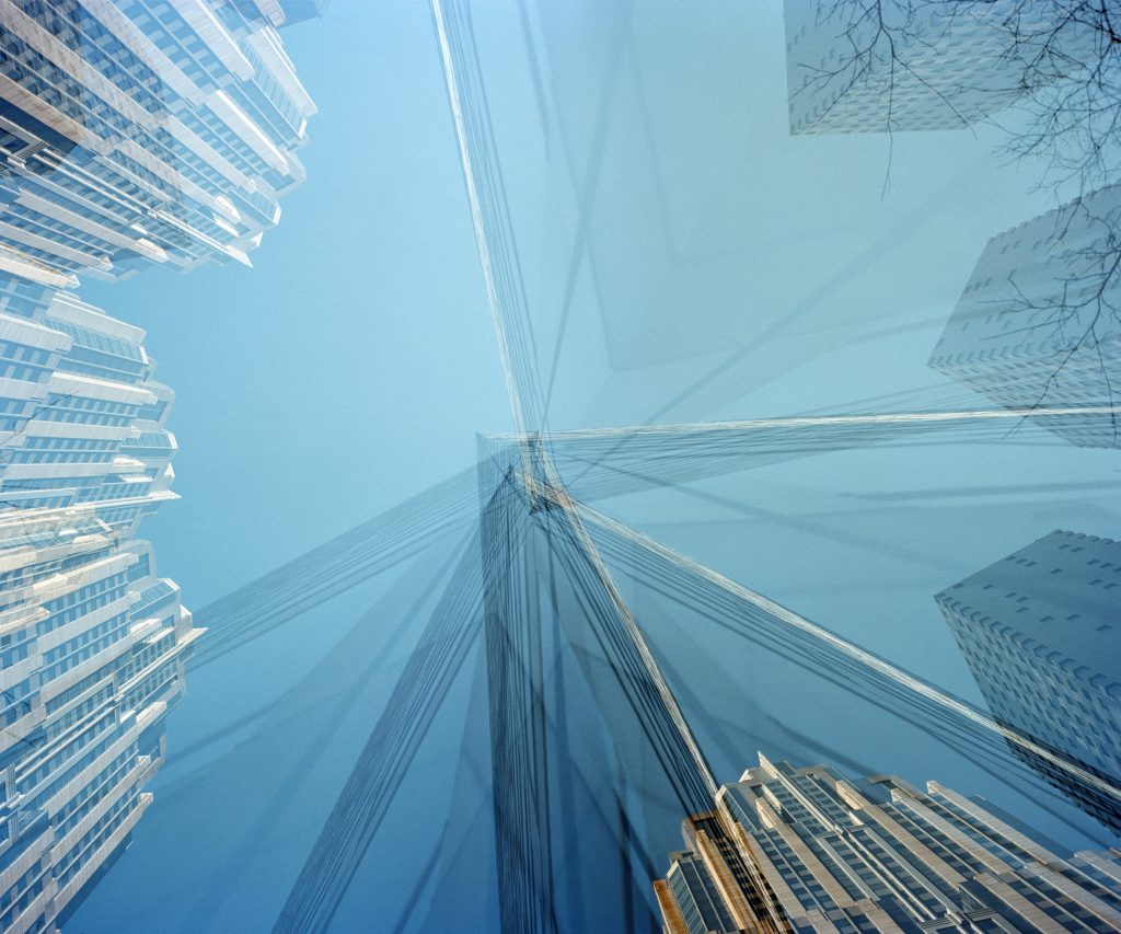 Kuvassa Nanna Hännisen teos On Fifth Avenue vuodelta 2010. Sinisävyisessä teoksessa on kuvattu korkeita rakennuksia pitkällä valotusajalla niin, että ne näykvät yhtäaikaa eri puolilla kuvaa. Kaikki rakennukset osoittavat kohti kuvan keskustaa.